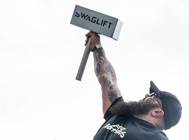 Two men in a&nbsp;tense armwrestling battle in front of a&nbsp;SWAGLIFT DAY banner